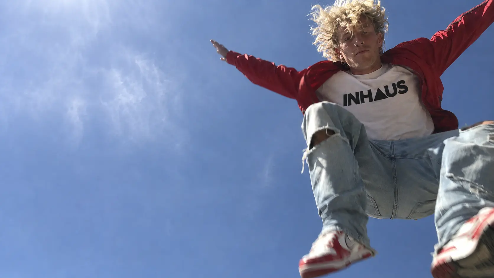 Blonde male artist leaping over a phone camera outdoors